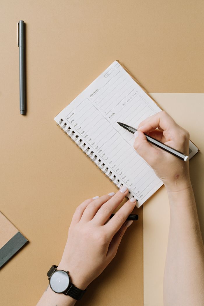 Close-up of hands writing in a planner on a brown desk, perfect for organizing and planning concepts.
